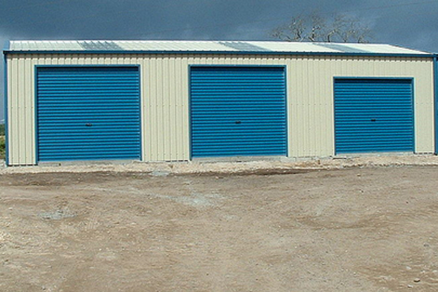 A cream building with three blue roller doors that are closed