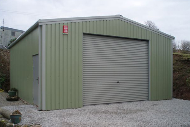 A green building with a roller door and personal access door at the side
